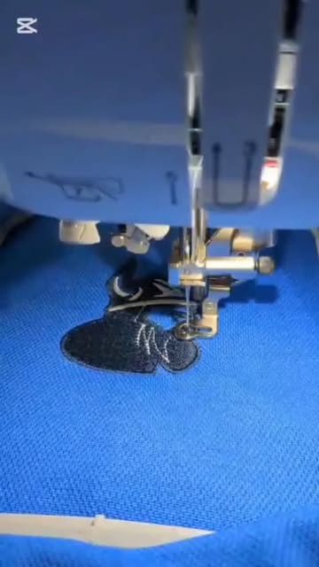 A dark silhouette design being embroidered on blue fabric